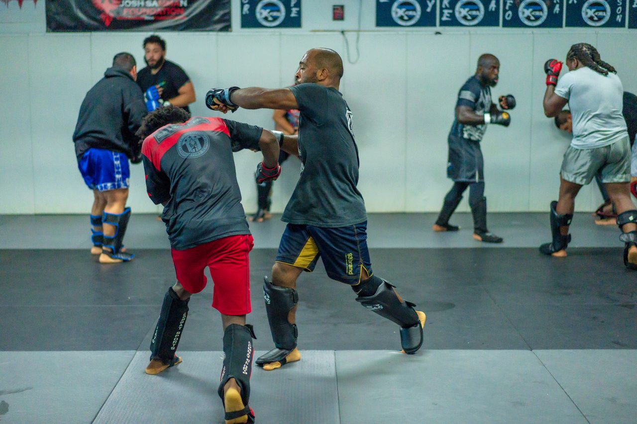 Men practicing martial arts and boxing in a gym, focusing on skill and technique.