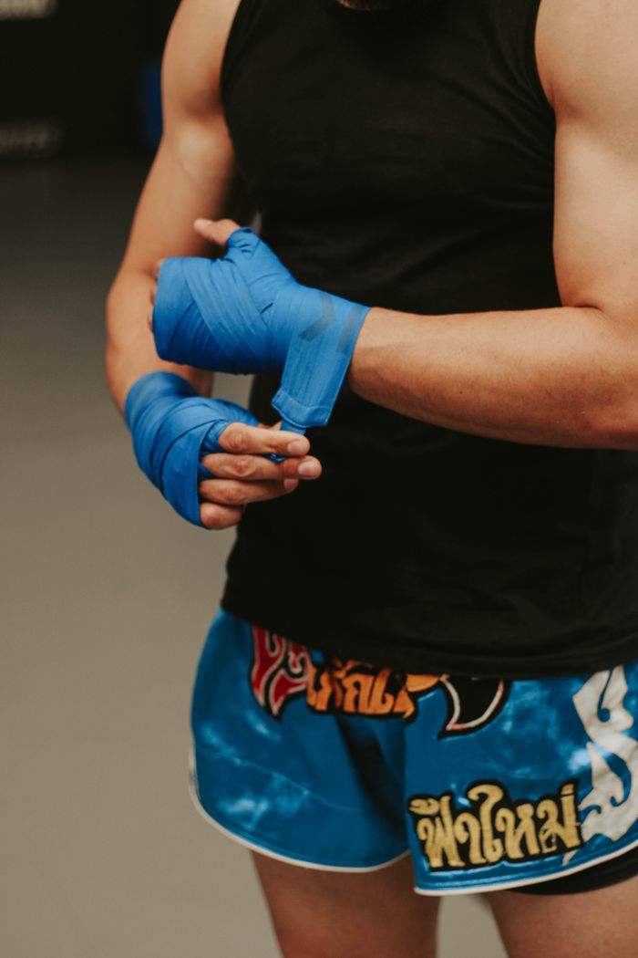 Services Crop faceless young male fighter in shorts wrapping boxing bandage before training in contemporary gym