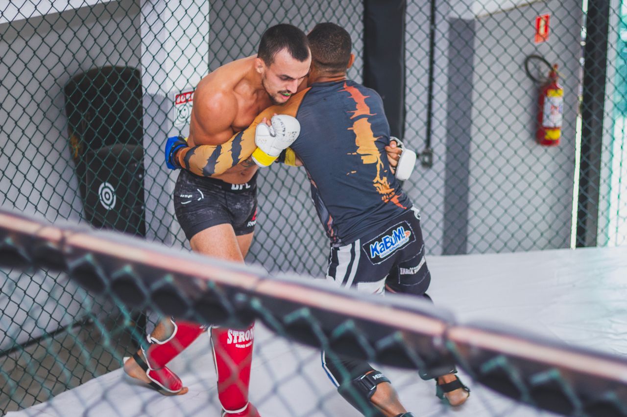 Home Two male athletes engaged in a competitive mixed martial arts training session in an indoor cage.